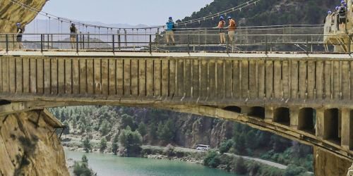 View of people crossing a bridge between cliffs, over the gorge with a river below.