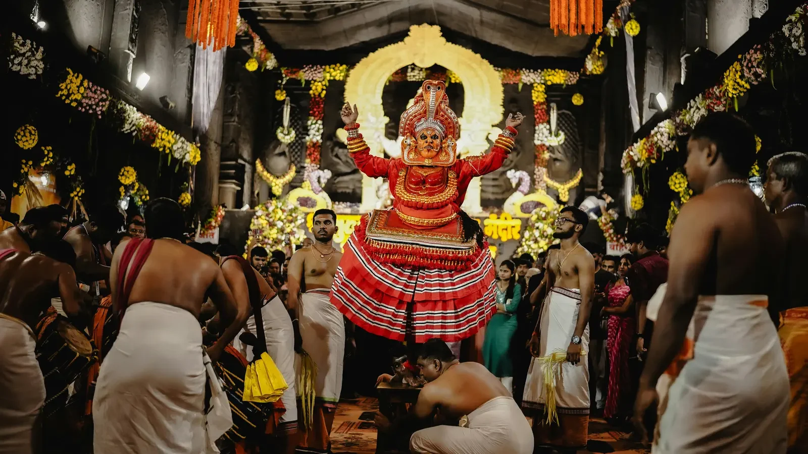 Artista de Theyyam en Kerala con maquillaje y tocado ritual, bendiciendo a los devotos durante una ceremonia