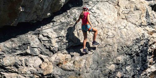 Picture of a young woman climbing along staples on a Via Ferrata.