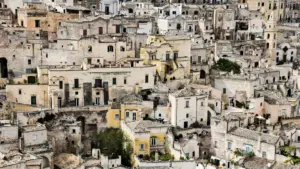Vista de edificios apilados en piedra en Matera, en tonos beige y arena, algunos oscurecidos por el tiempo, con pocos árboles dispersos