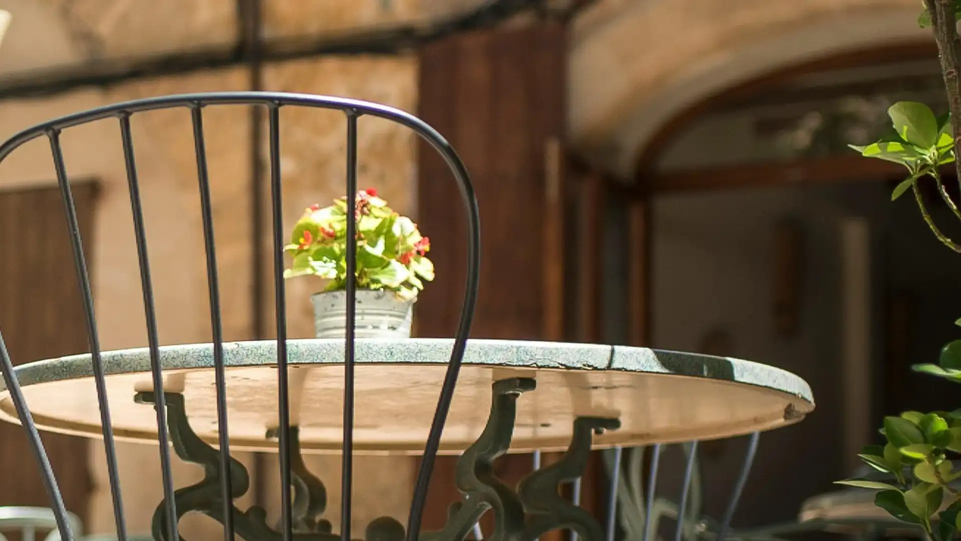 Sunlit courtyard in Mallorca with a rustic table and metal chair, perfect for quiet escapes and Mediterranean charm.