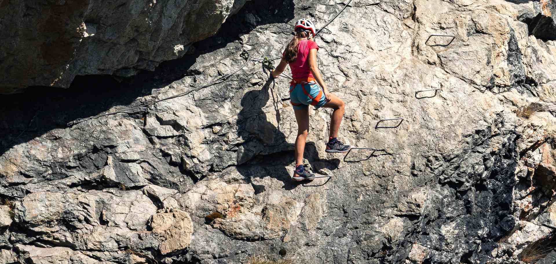 Picture of a young woman climbing along staples on a mountain face.